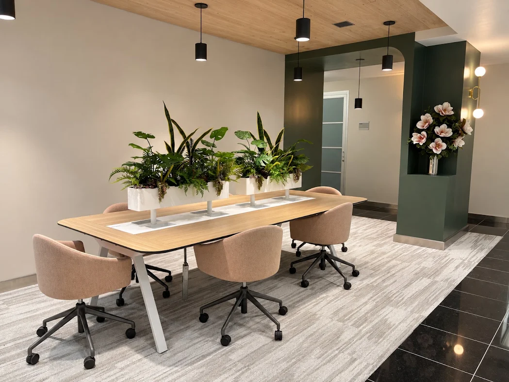 Shared coworking table with upholstered chairs and plants at Jay Suites